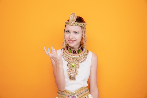 고대 이집트 의상을 입은 클레오파트라 같은 아름다운 여성, 오렌지색에 대한 공격적인 표정으로 화가 난 얼굴로 팔을 들고 있다