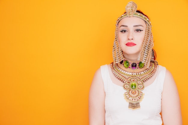 オレンジ色に真剣に自信を持って表現する古代エジプトの衣装を着たクレオパトラのような美しい女性