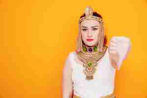 Бесплатное фото Красивая женщина, как клеопатра в древнем египетском костюме, недовольна, показывая большой палец на апельсине