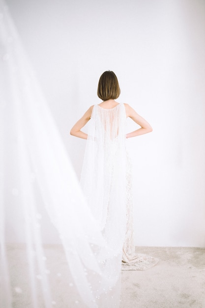 Free photo beautiful woman in long white dress standing in room with white walls