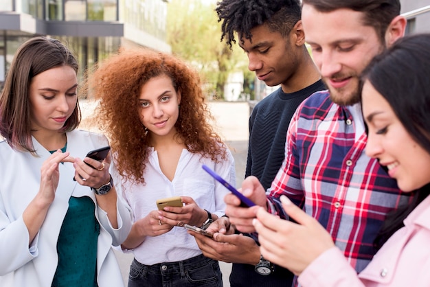 Beautiful woman looking at camera standing between her friends using cell phones