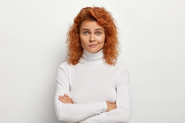 Beautiful woman looks with attention at camera, keeps arms folded