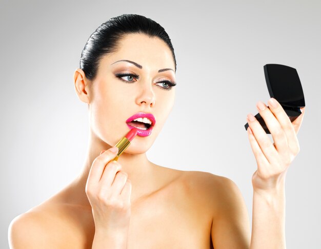 Красивая женщина делает макияж, применяя розовую помаду на губах.