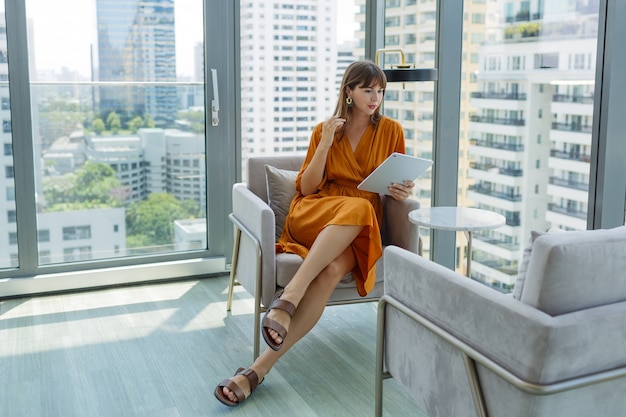 Красивая женщина в оранжевом платье с помощью планшета в современном офисе на крыше.