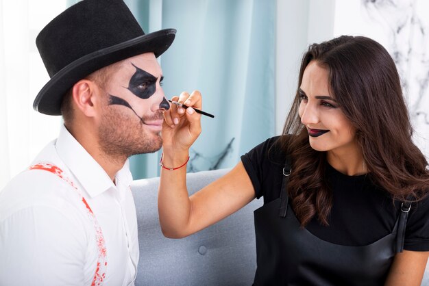 Beautiful woman painting husbands face for halloween