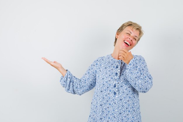 Beautiful woman in patterned blouse pointing at someone while laughing and looking cheery , front view.