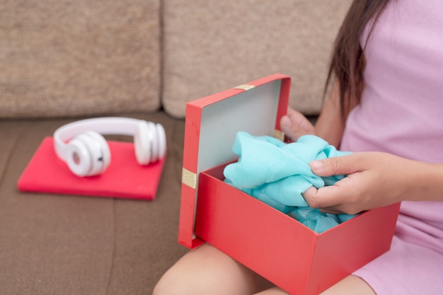 Beautiful woman in pink dress, sitting on the sofa, opening a gift box.