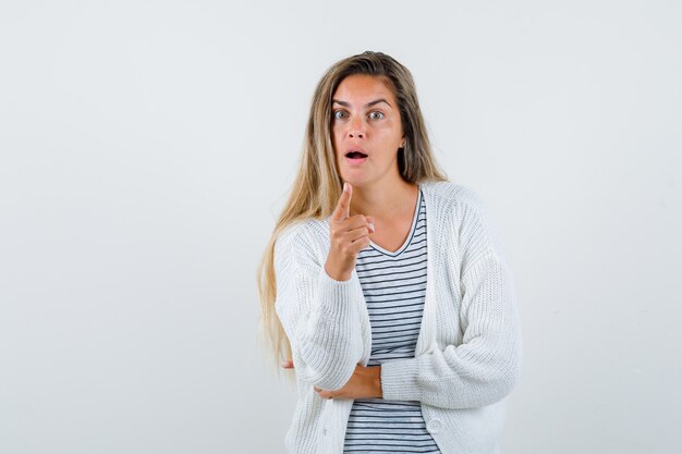 Beautiful woman pointing at camera in jacket and looking surprised , front view.