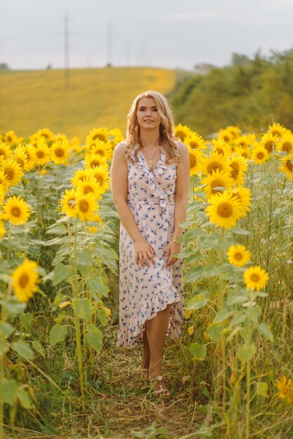 Красивая женщина позирует на сельскохозяйственном поле с подсолнухом в солнечный летний день