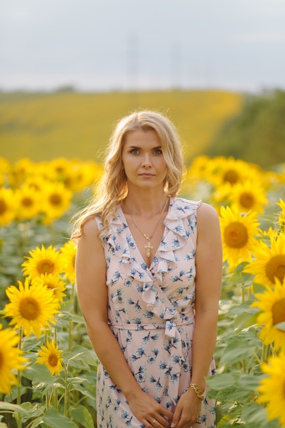 Beautiful woman poses in the agricultural field with sunflower on a sunny summer day