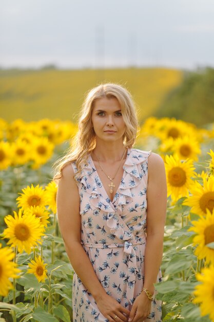 Beautiful woman poses in the agricultural field with sunflower on a sunny summer day