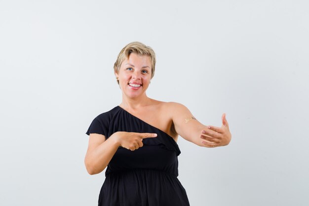 Beautiful woman posing like holding phone while pointing at it in black blouse and looking glad.