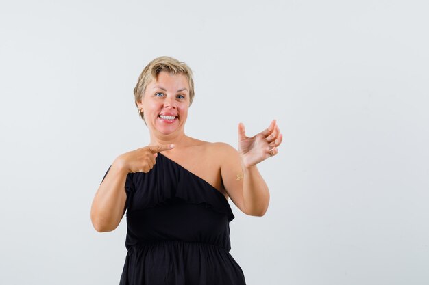 Beautiful woman posing like pointing at phone in black blouse and looking pleased.