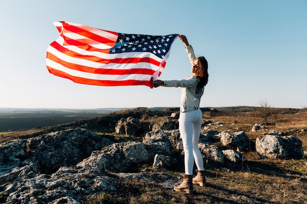 Красивая женщина позирует с американским флагом на вершине горы