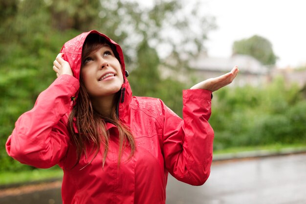 雨をチェックするレインコートの美しい女性