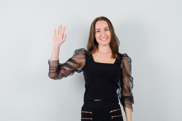 Beautiful woman raising hand up in black blouse and looking cheery. front view.