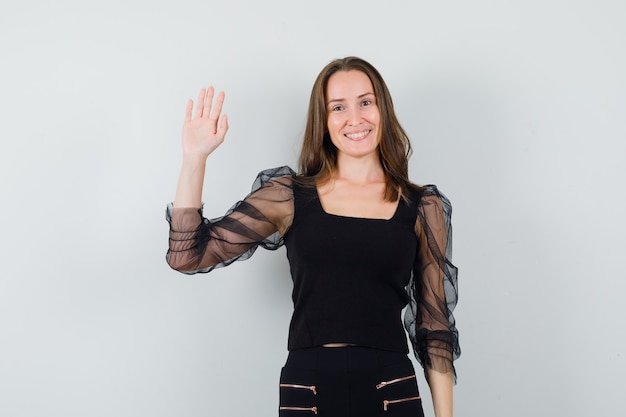 Beautiful woman raising hand up in black blouse and looking cheery. front view.