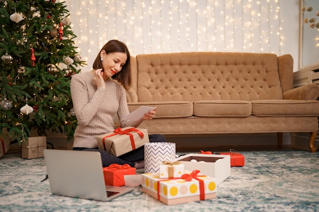 선물 상자 사이에 앉아있는 동안 크리스마스 인사말 카드를 읽고 아름 다운 여자.