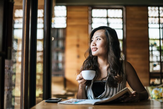 美しい女性のカフェで雑誌を読む