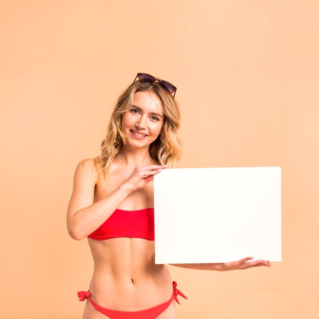 Beautiful woman in red swimsuit showing blank paper