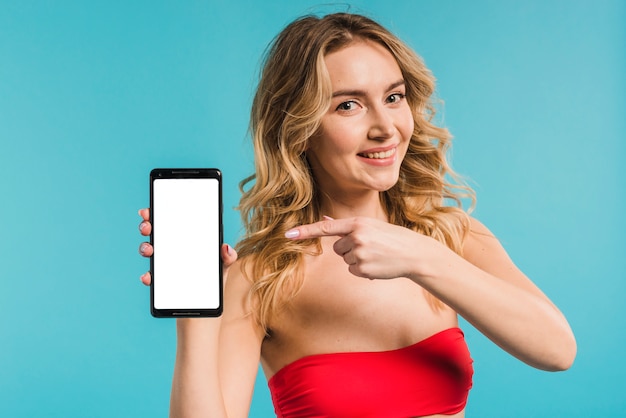 Free photo beautiful woman in red top holding and pointing to mobile phone