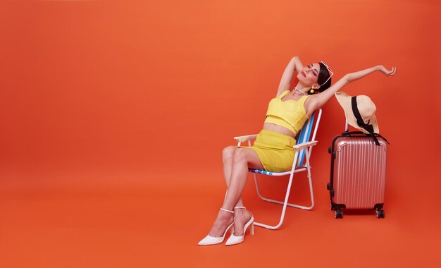 Beautiful woman relax sitting on a beach chair with suitcase in studio summer orange background