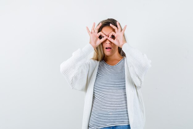 Beautiful woman showing glasses gesture in jacket and looking surprised , front view.