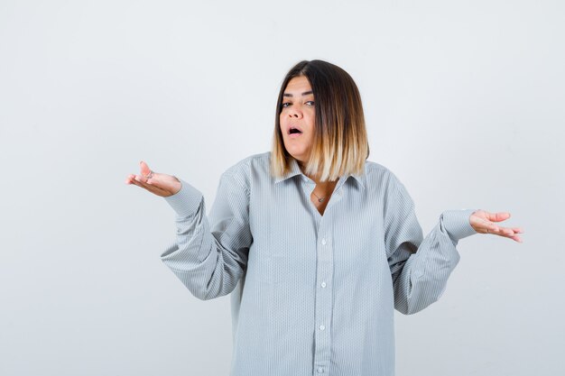 Beautiful woman showing helpless gesture in shirt and looking puzzled , front view.