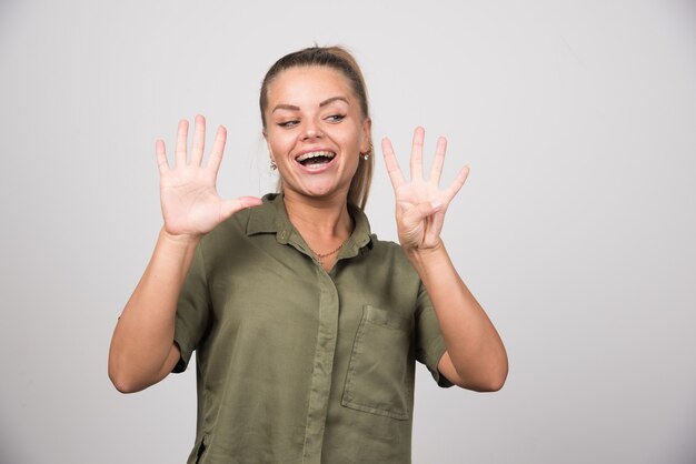 Beautiful woman showing her fingers on gray wall.