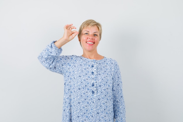 Free photo beautiful woman showing ok gesture in patterned blouse and looking jolly. front view.