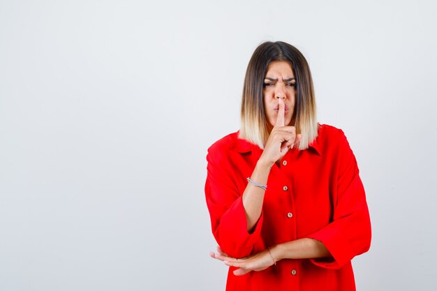 Beautiful woman showing silence gesture in red blouse and looking serious , front view.