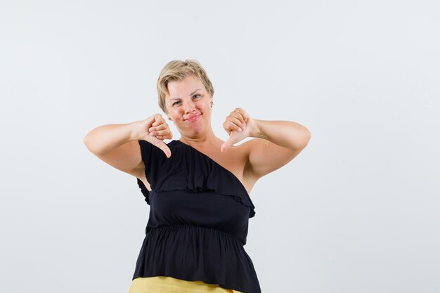 Beautiful woman showing thumb down in black blouse and looking discontented.