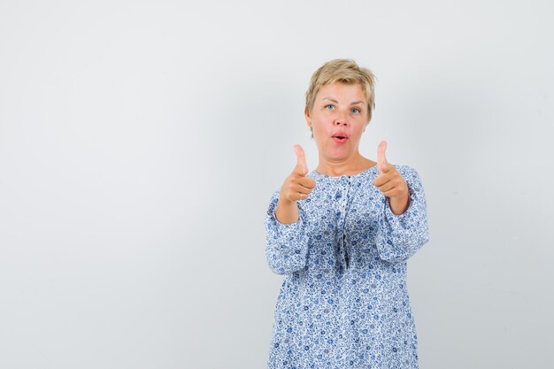 Beautiful woman showing thumb up in patterned blouse and looking pleased. front view. space for text