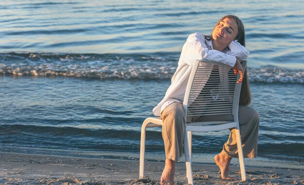 A beautiful woman sits on a chair near the sea