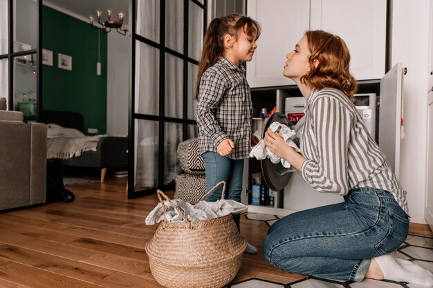 Beautiful woman sits on floor and wipes lid off pan while her little daughter speaks to her.