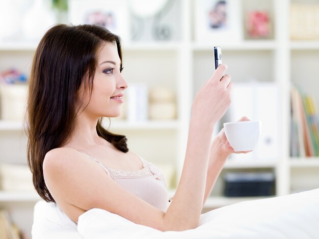 Beautiful woman sitting at home with cup and mobile and reading a messege