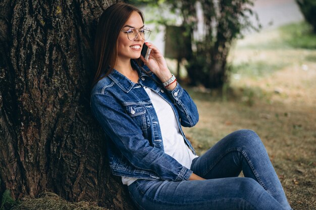 아름 다운 여자는 나무 아래 앉아 전화 통화