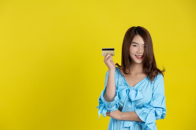 Beautiful woman smiling at camera and holding credit card on yellow wall