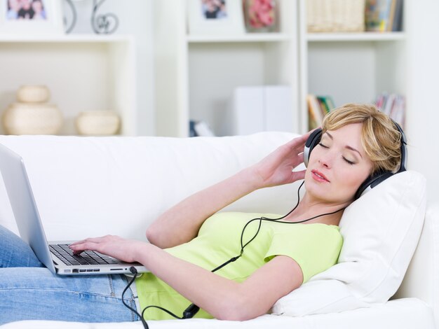 Beautiful woman  in the sofa with  laptop  listening music in headphone - indoors