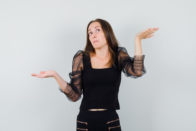 Beautiful woman spreading open palms aside in black blouse and looking puzzled 