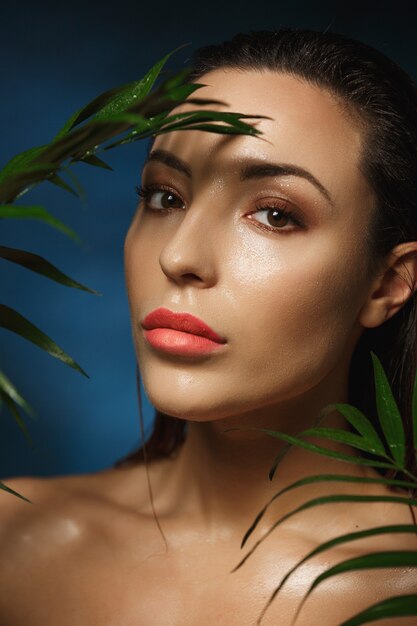 Beautiful woman standing under green leaves shirtless. After rain.