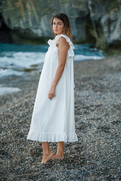 立っていると日没時に白いドレスの海岸で探していると悲しい探している美しい女性。 。