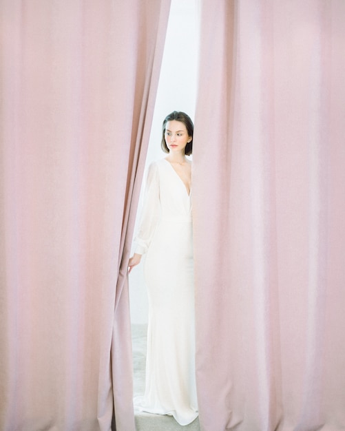 Красивая женщина стоя и думая в длинном белом платье в комнате жемчуга.