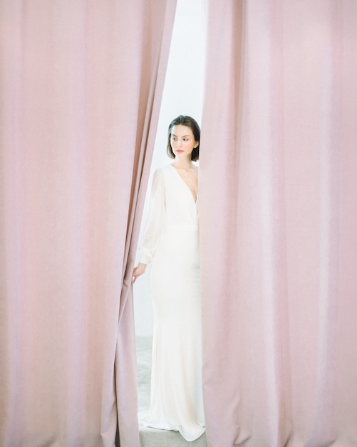 Beautiful woman standing and thinking in long white dress in pearl room .