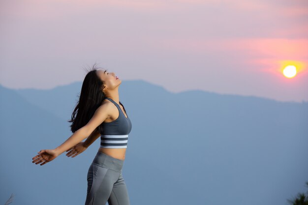 일몰에 산에 그녀의 팔으로 서 아름 다운 여자