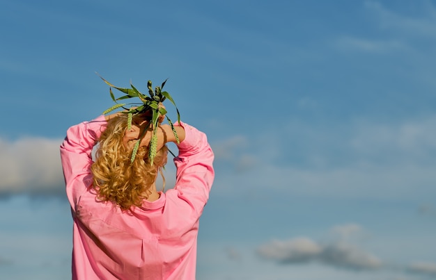 Beautiful woman stands with her back to the frame, in her hands above her head ears of wheat. Blue sky with clouds, selective focus with copy space, idea for a banner or background