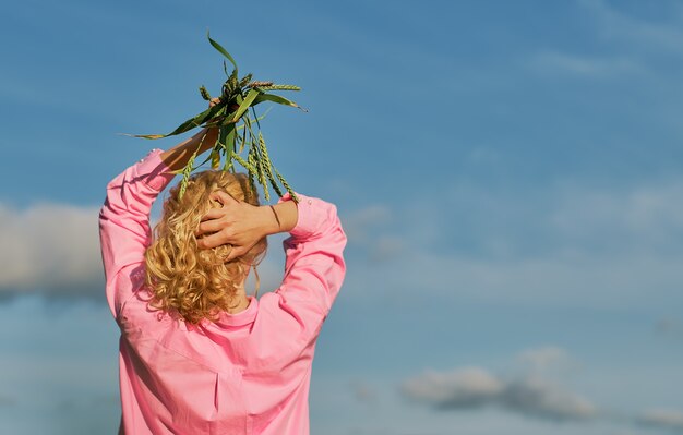 Красивая женщина стоит спиной к кадру, в руках над головой колосья пшеницы. голубое небо с облаками, выборочный фокус с копией пространства, идея для баннера или фона