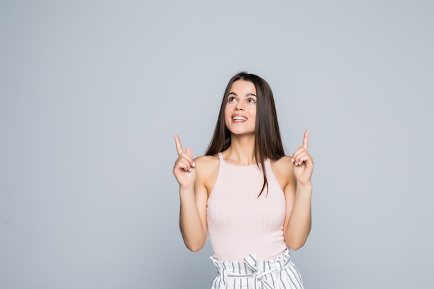 Beautiful woman student raising hands high and pointing up with index fingers isolated on gray wall