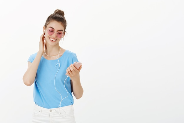 Beautiful woman in sunglasses listening music in earphones, using mobile phone