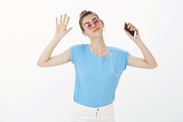 Красивая женщина в солнцезащитных очках, слушая музыку в наушниках, используя мобильный телефон